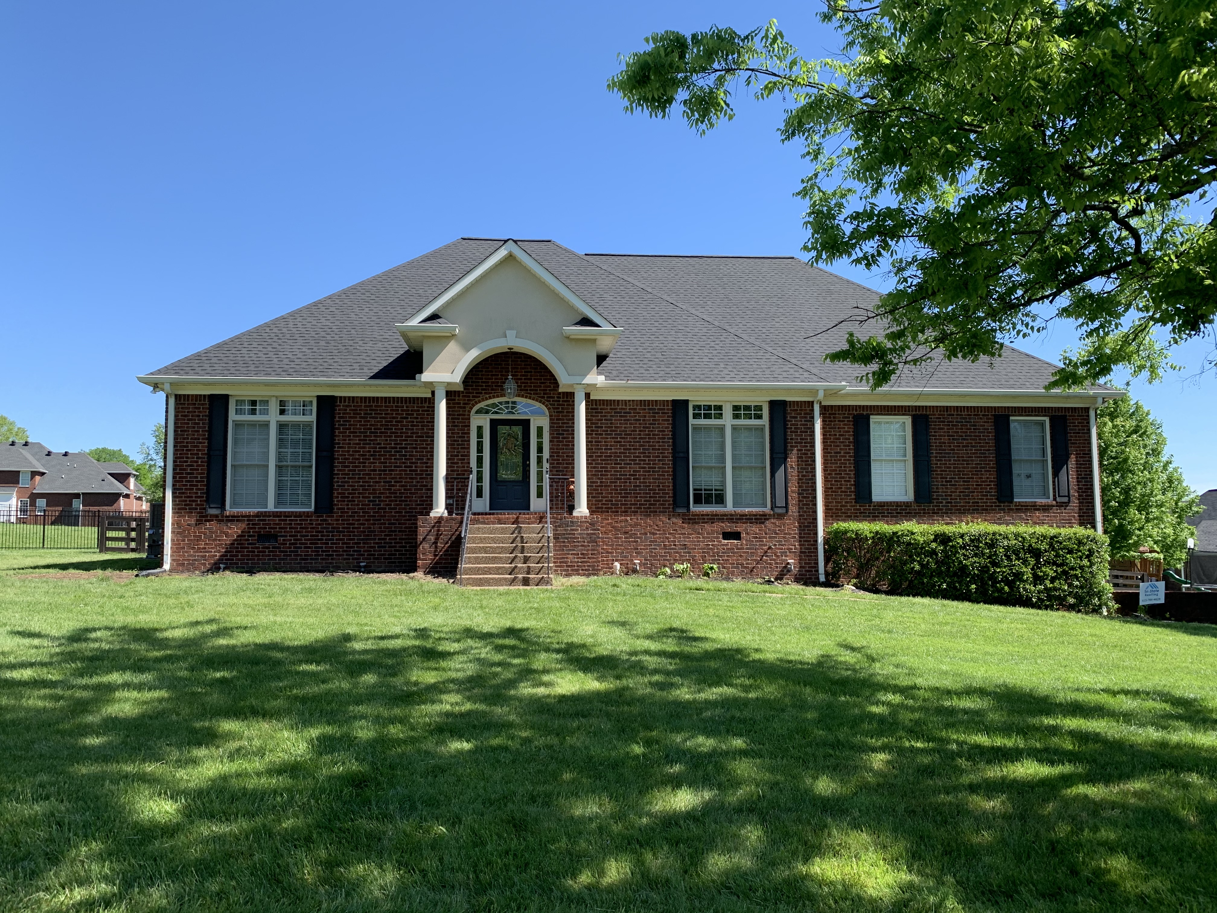 red brick home with dark grey / black roof and green grass in Lebanon TN